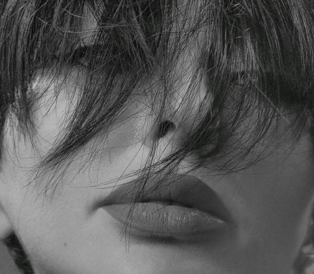 Monochrome close-up portrait of a woman with hair covering face, conveying mystery.