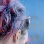 Close-up view of vibrant pink and purple dyed hair against a blue background.
